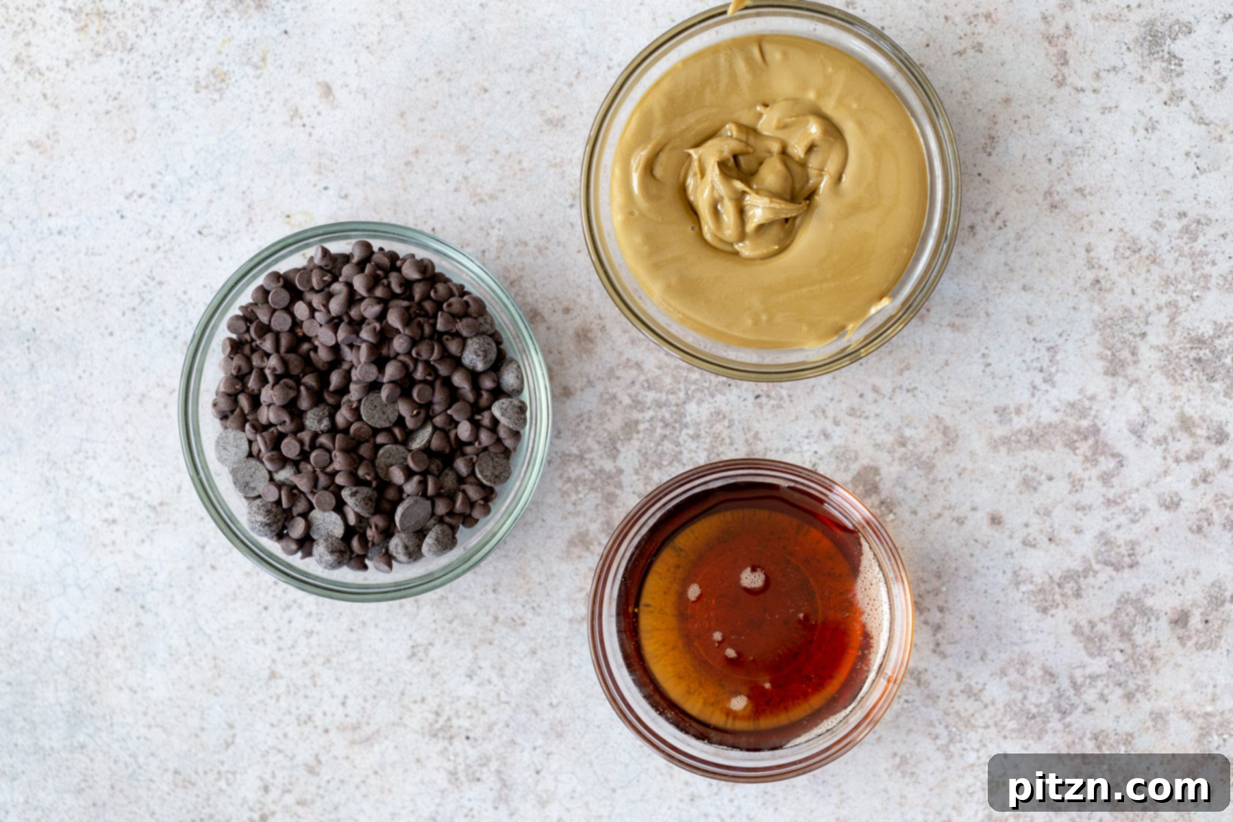 Collection of ingredients laid out on a kitchen counter, including chocolate chips, a jar of nut butter, and maple syrup, ready for making vegan chocolate fudge.
