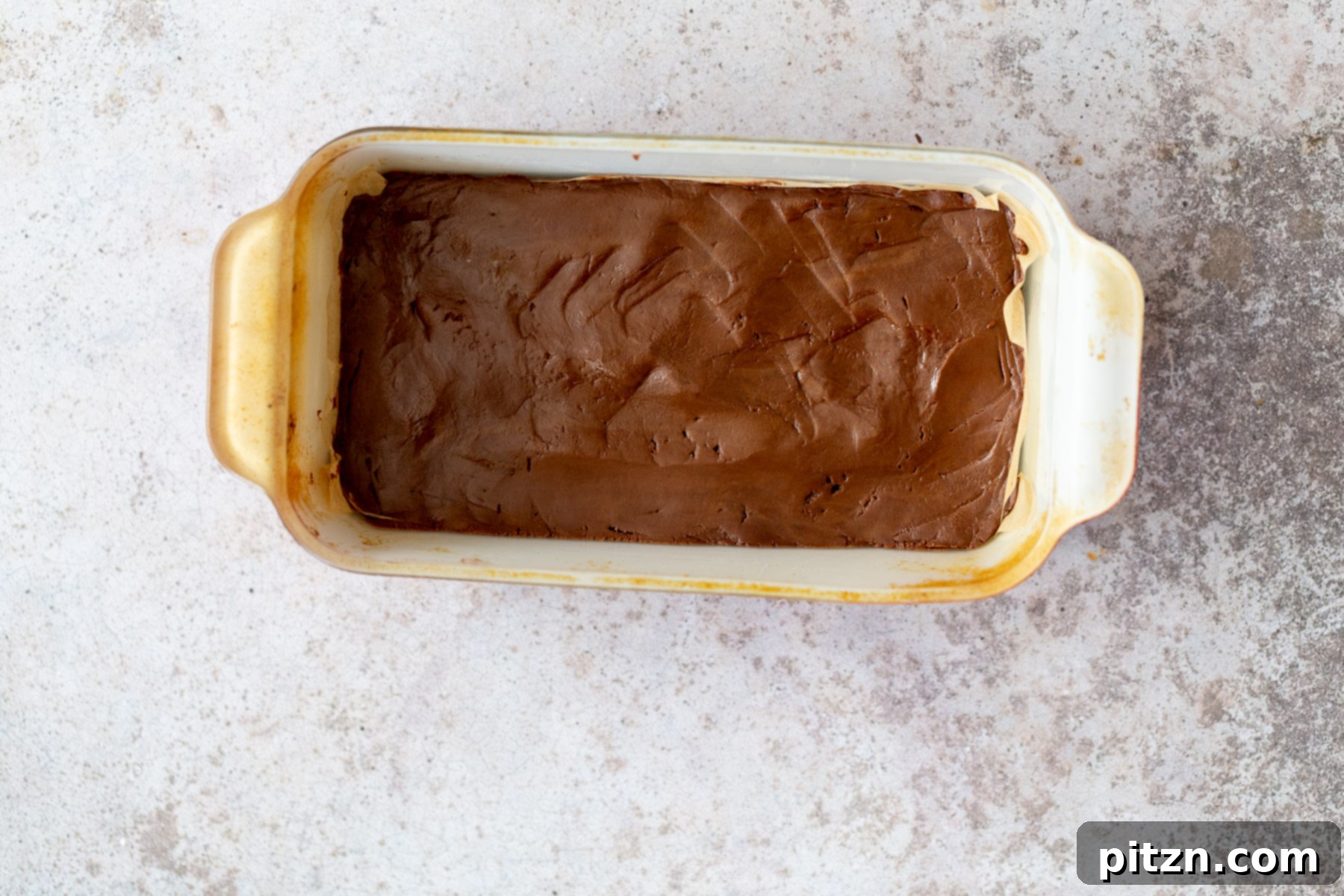 Set vegan chocolate fudge in a white loaf pan, lined with parchment paper, ready to be chilled and then sliced. The surface is smooth and uniform.
