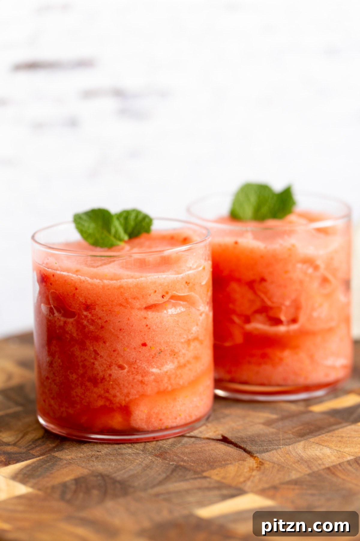 Two glasses of homemade vegan strawberry lemonade slushies, garnished with mint, resting on a rustic wooden board.