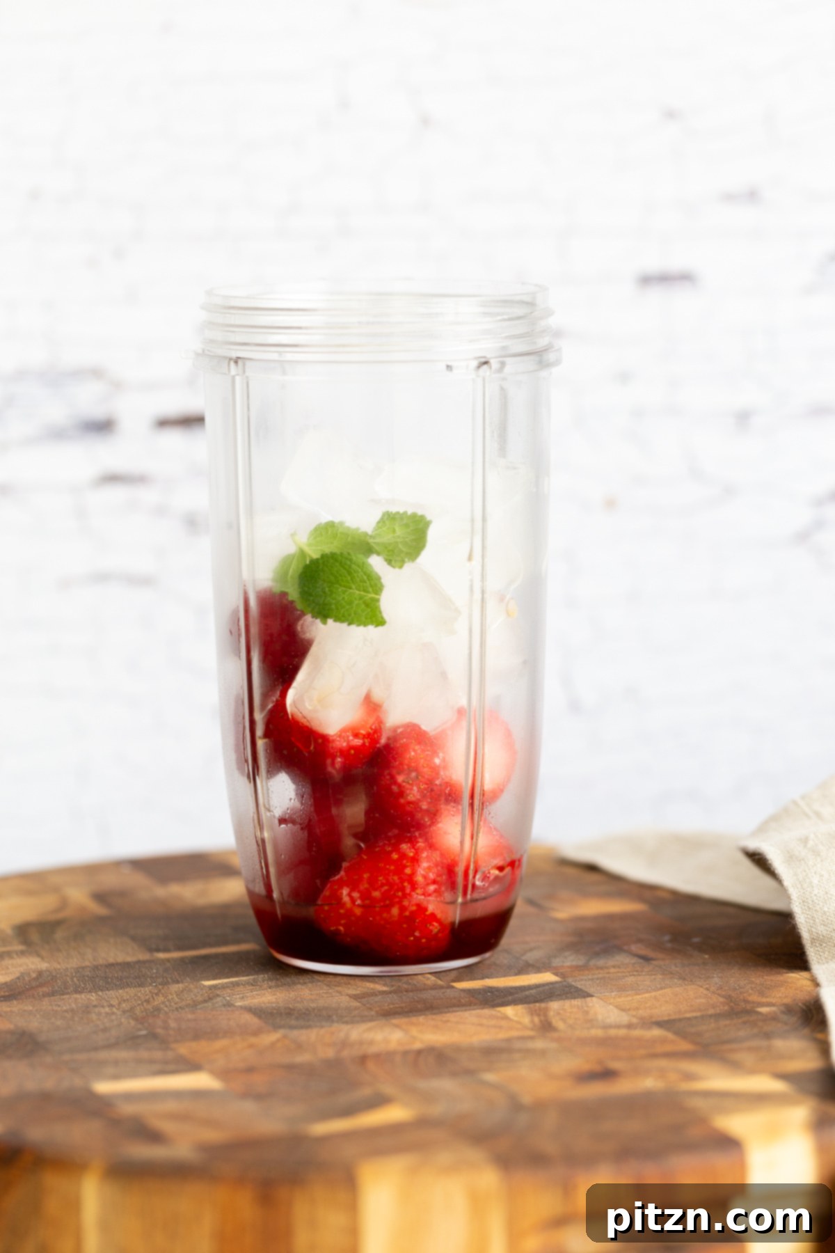 Close-up shot of ice cubes, fresh mint leaves, and vibrant frozen strawberries, all loaded into a blender, ready for mixing.