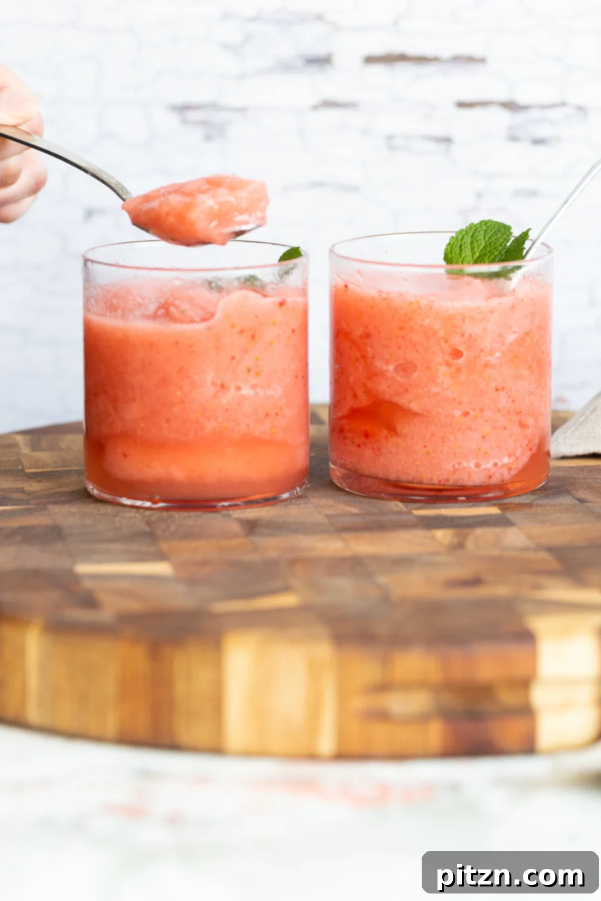 Two beautifully presented homemade vegan strawberry lemonade slushies, garnished with fresh mint, arranged on a rustic wooden board, ready to be enjoyed.