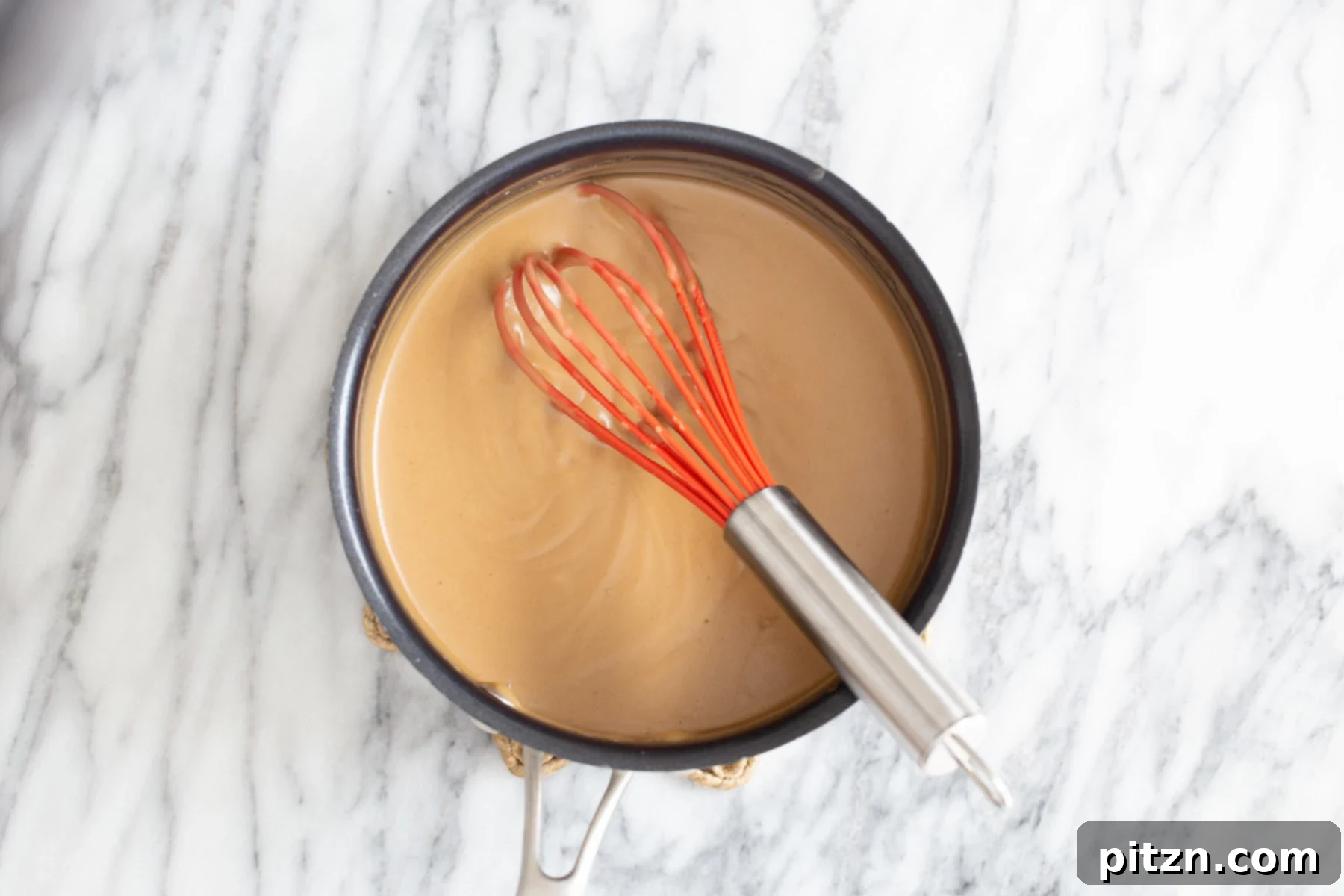 Peanut butter mousse base being whisked in a saucepan with a red whisk