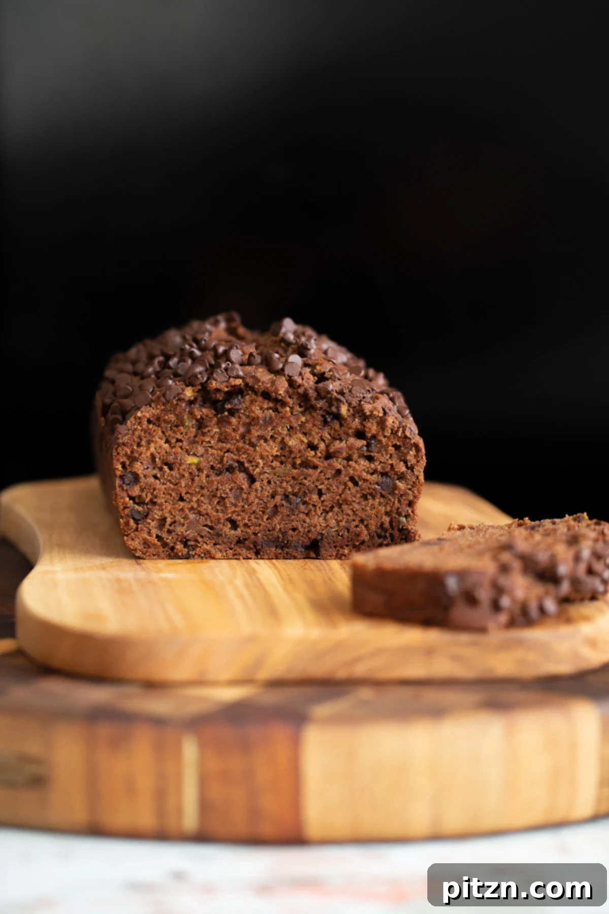 A sliced loaf of moist vegan chocolate zucchini bread on a rustic wooden chopping board, showcasing its rich texture and chocolate chips.