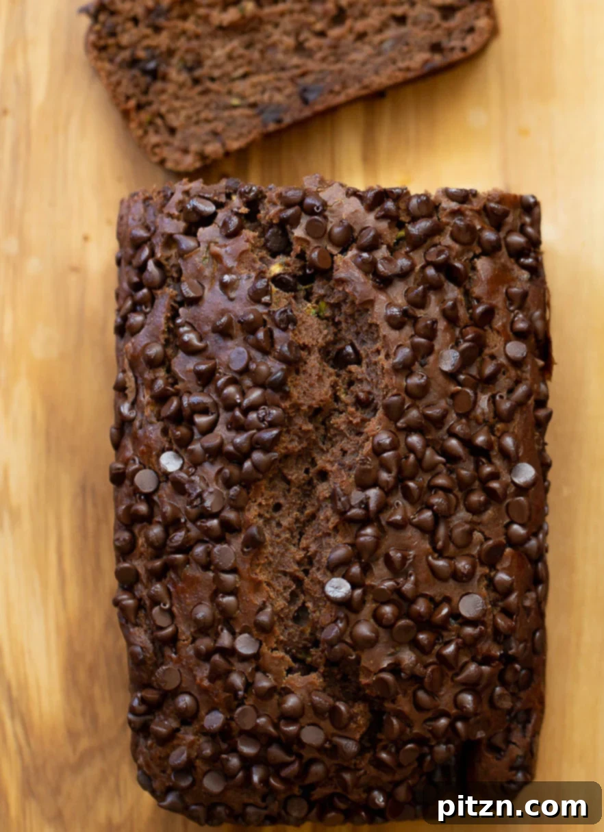 An overhead shot of a freshly baked loaf of vegan chocolate zucchini bread on a chopping board, highlighting its golden-brown crust and inviting texture.
