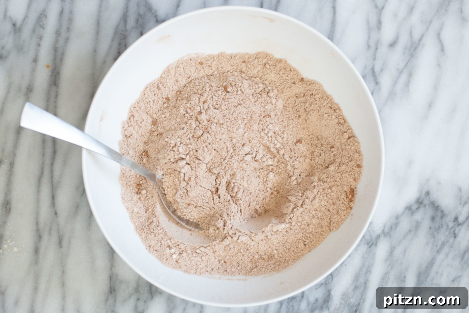 Dry ingredients for vegan chocolate zucchini bread, including flour, cocoa, and spices, mixed in a white bowl.