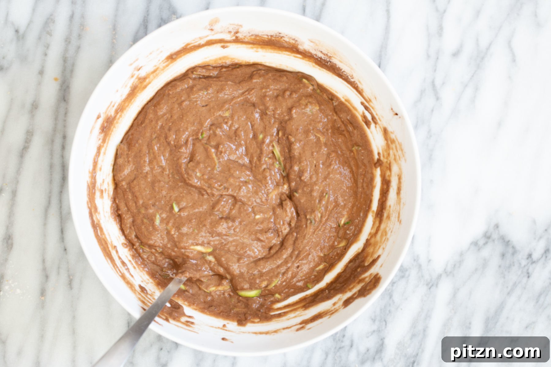 Smooth, rich chocolate zucchini cake batter in a white bowl, showing its thick and ready consistency before adding mix-ins.