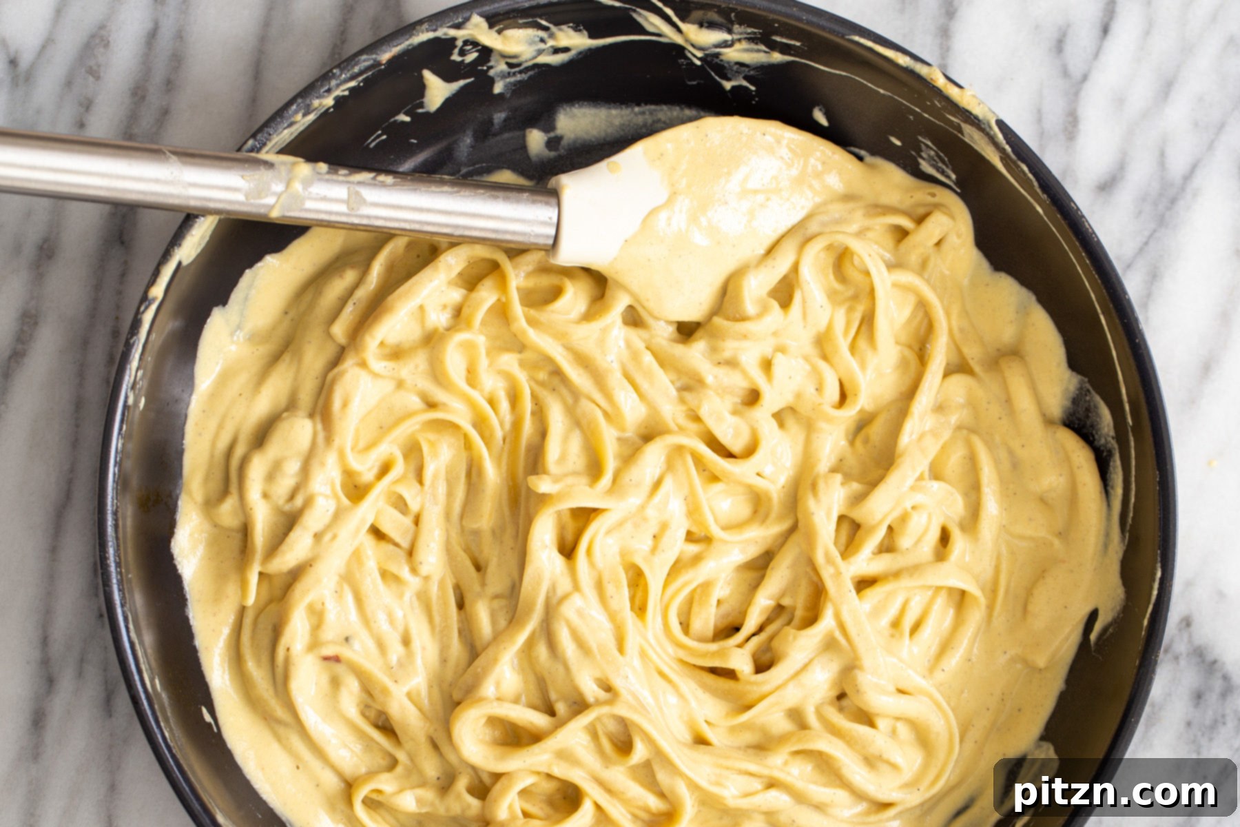fettuccine being tossed in vegan butternut squash cashew cheese carbonara sauce