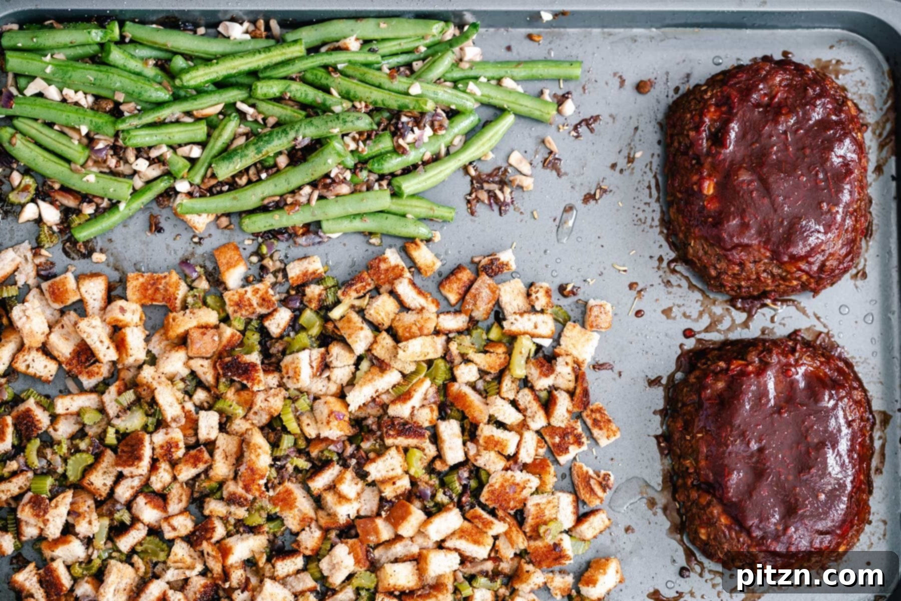 Baked Vegan Stuffing and Green Beans A full view of the baked vegan stuffing and vibrant green beans, positioned next to two small, glazed lentil meatloaves on a single sheet pan.