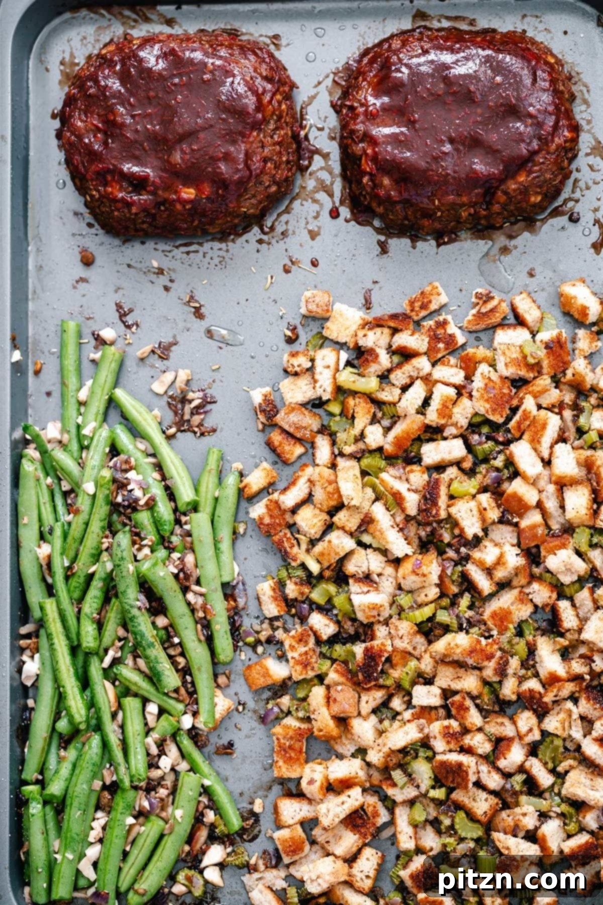 Complete Thanksgiving Sheet Pan Meal An inviting view of the Thanksgiving sheet pan dinner, featuring two golden lentil loaves, fluffy vegan stuffing, and bright green beans ready to be served.