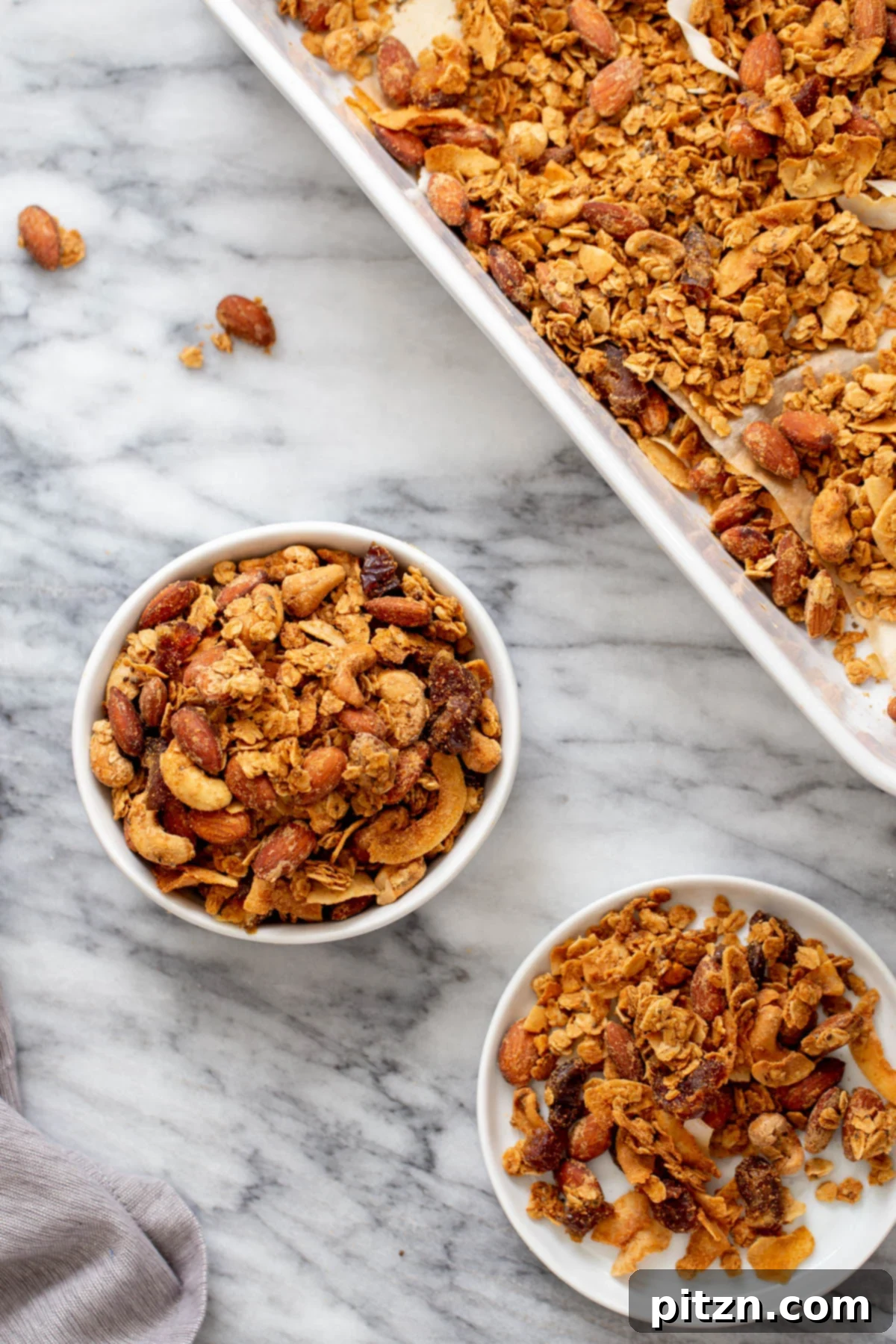 Homemade Coconut Almond Granola Two small bowls of homemade baked vegan almond coconut granola next to a baking sheet with granola