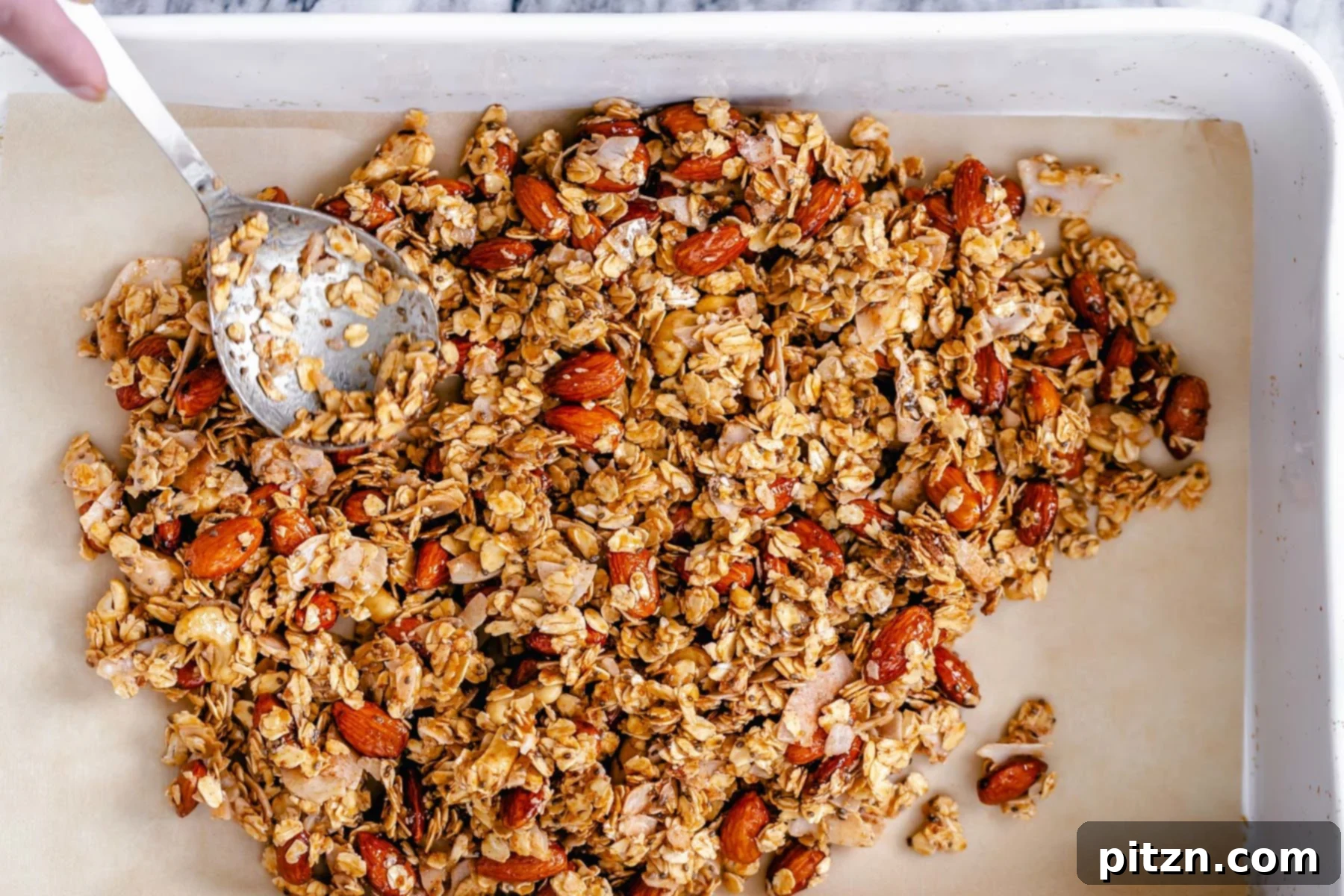 Spreading Granola on Baking Tray Almond coconut granola being spread onto a baking tray to make baked vegan coconut granola