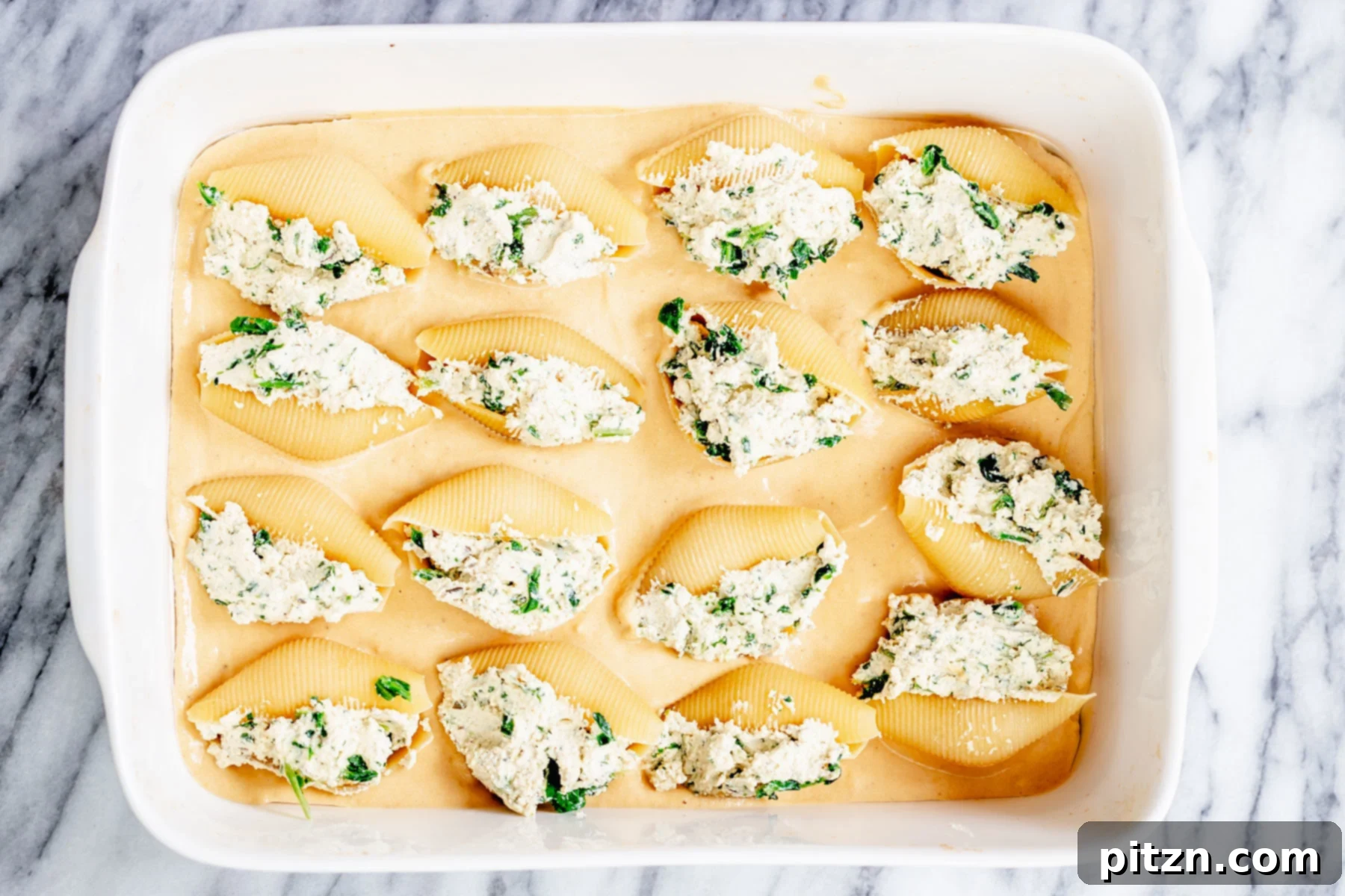 Assembling the Casserole Overhead shot of vegan tofu ricotta stuffed shells arranged on a bed of butternut squash alfredo in a baking dish.