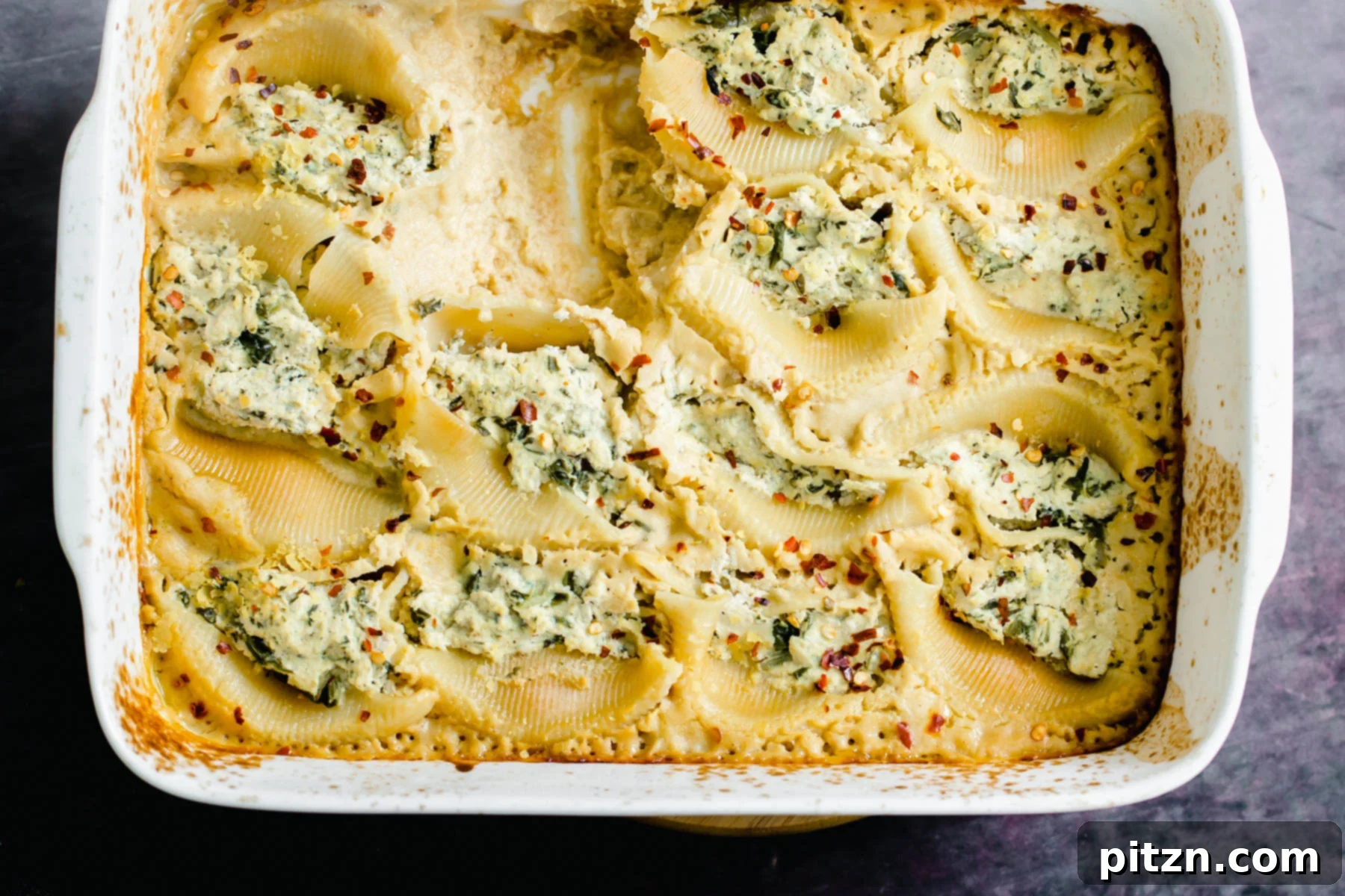 Garnished Vegan Stuffed Shells Overhead shot of a casserole dish filled with golden-brown vegan ricotta stuffed shells in butternut alfredo, garnished.