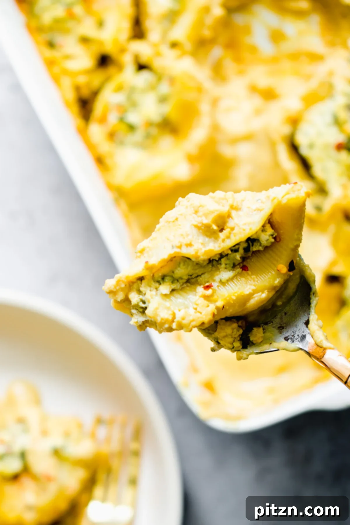Delicious Vegan Stuffed Shells Close-up of a spoon scooping a perfectly baked vegan stuffed shell, showcasing the creamy tofu ricotta filling.