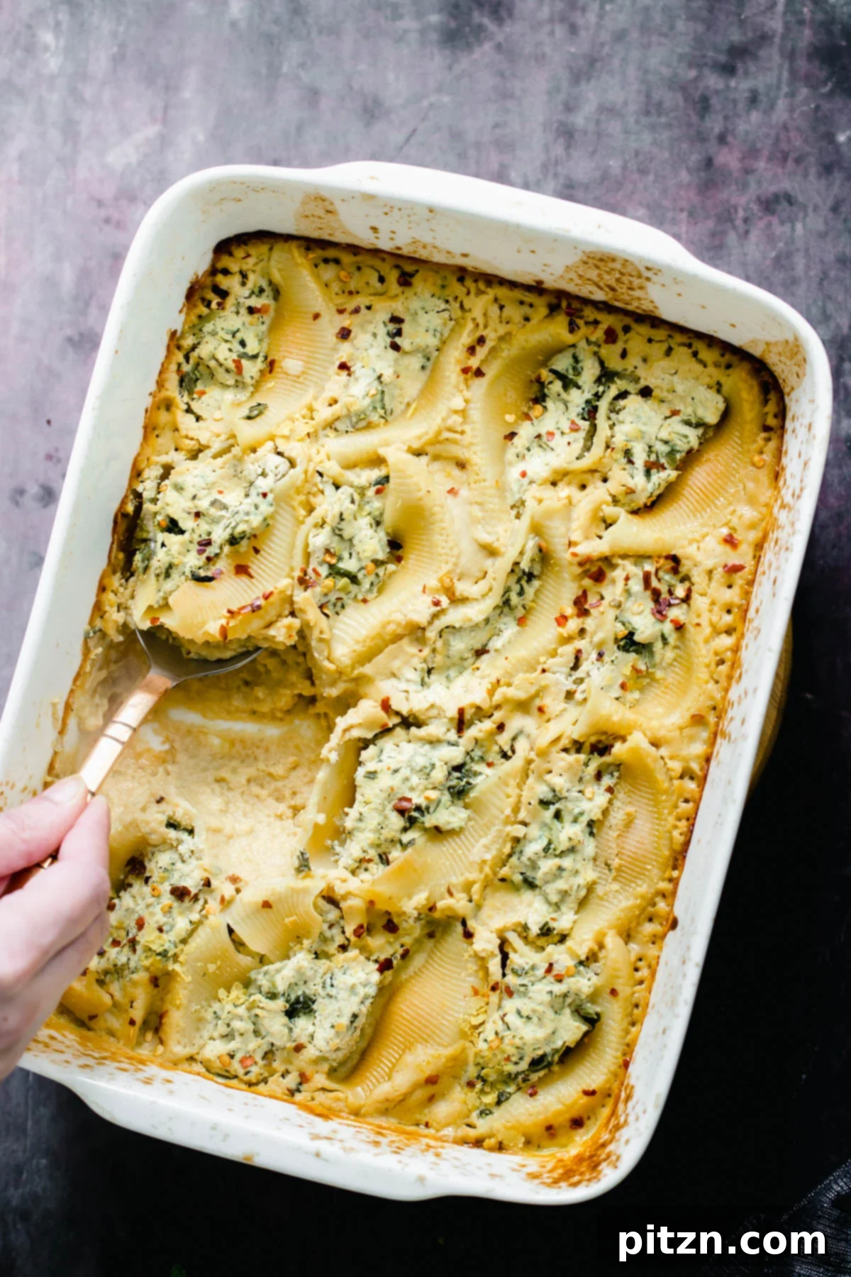 Serving Vegan Stuffed Shells A silver serving spoon lifting a portion of vegan ricotta stuffed shells from a casserole dish, ready to be served.