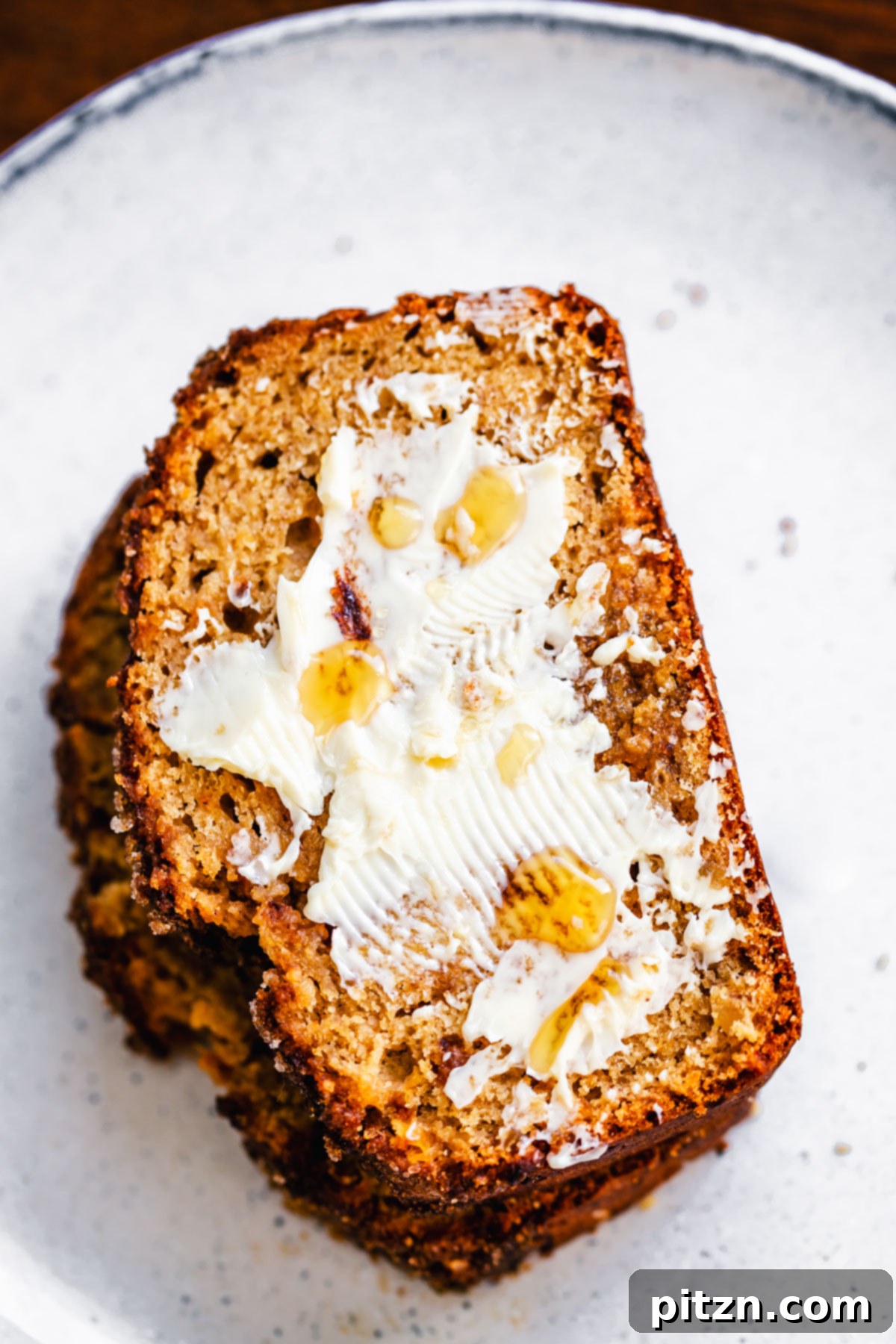 A single slice of buttered vegan gingerbread banana bread on a white plate, ready to be enjoyed.