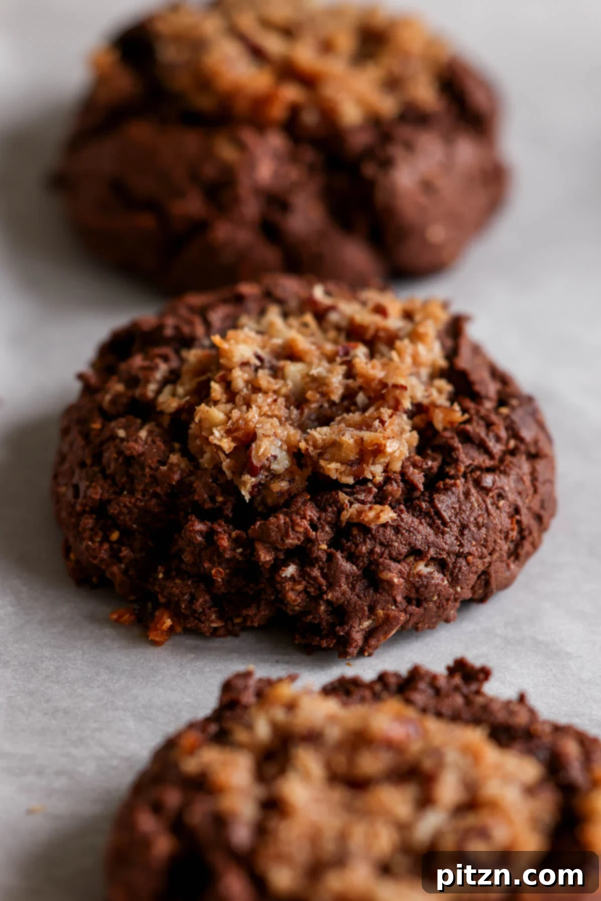 Freshly baked vegan German chocolate cookies cooling on a baking sheet, showcasing their rich color and inviting texture.