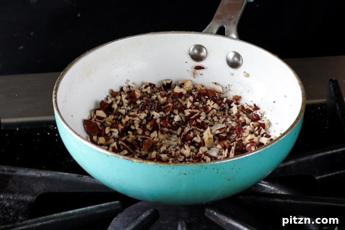 Chopped pecans toasting in a skillet on the stovetop, releasing their aromatic oils and deepening in color.