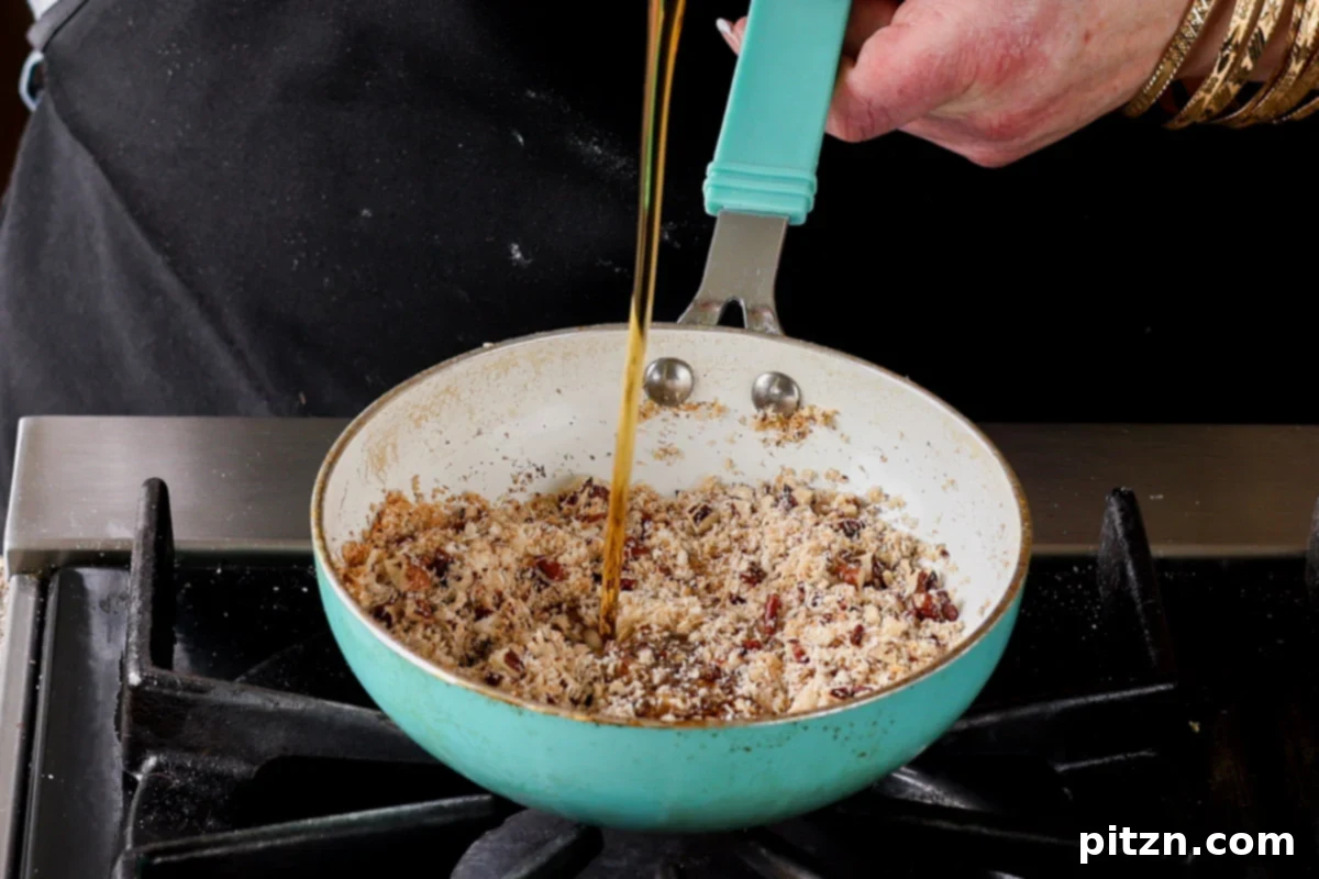Maple syrup being poured into the skillet with toasted coconut and pecans, initiating the caramelization process for the filling.