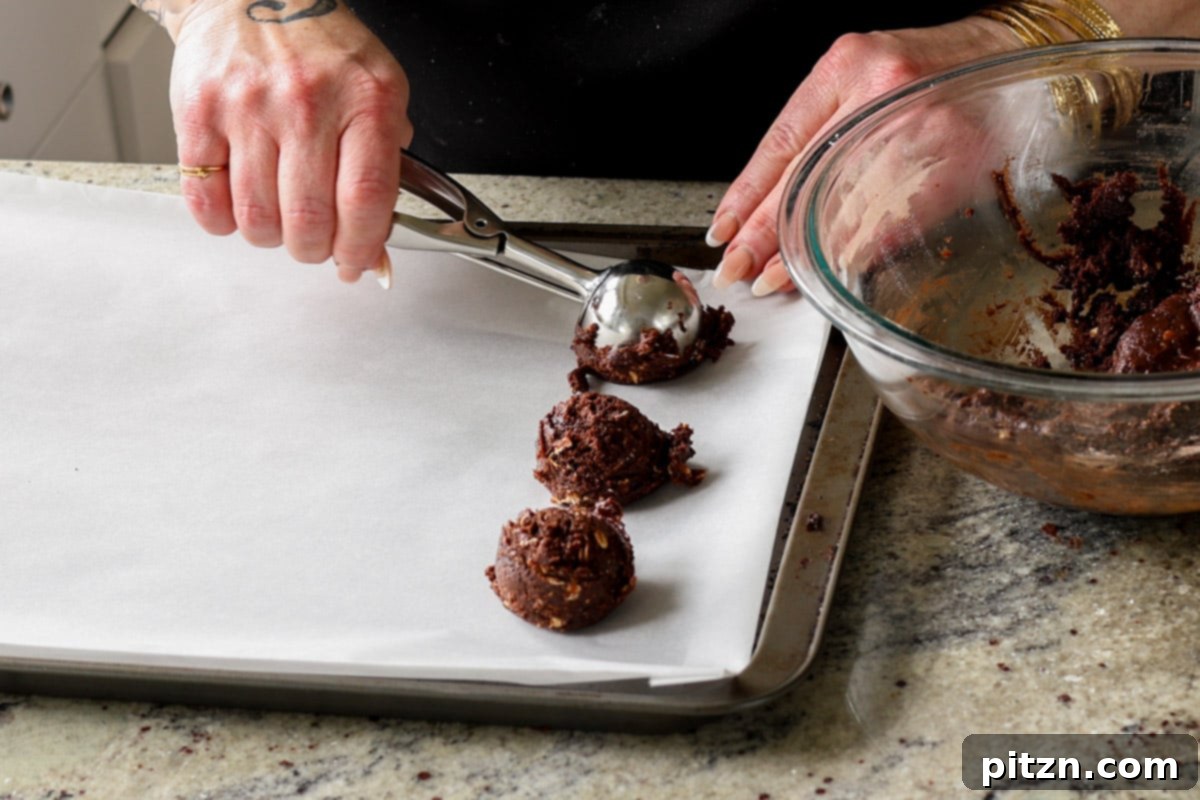Scooping portions of chocolate cookie dough onto a parchment-lined baking sheet, preparing for shaping.