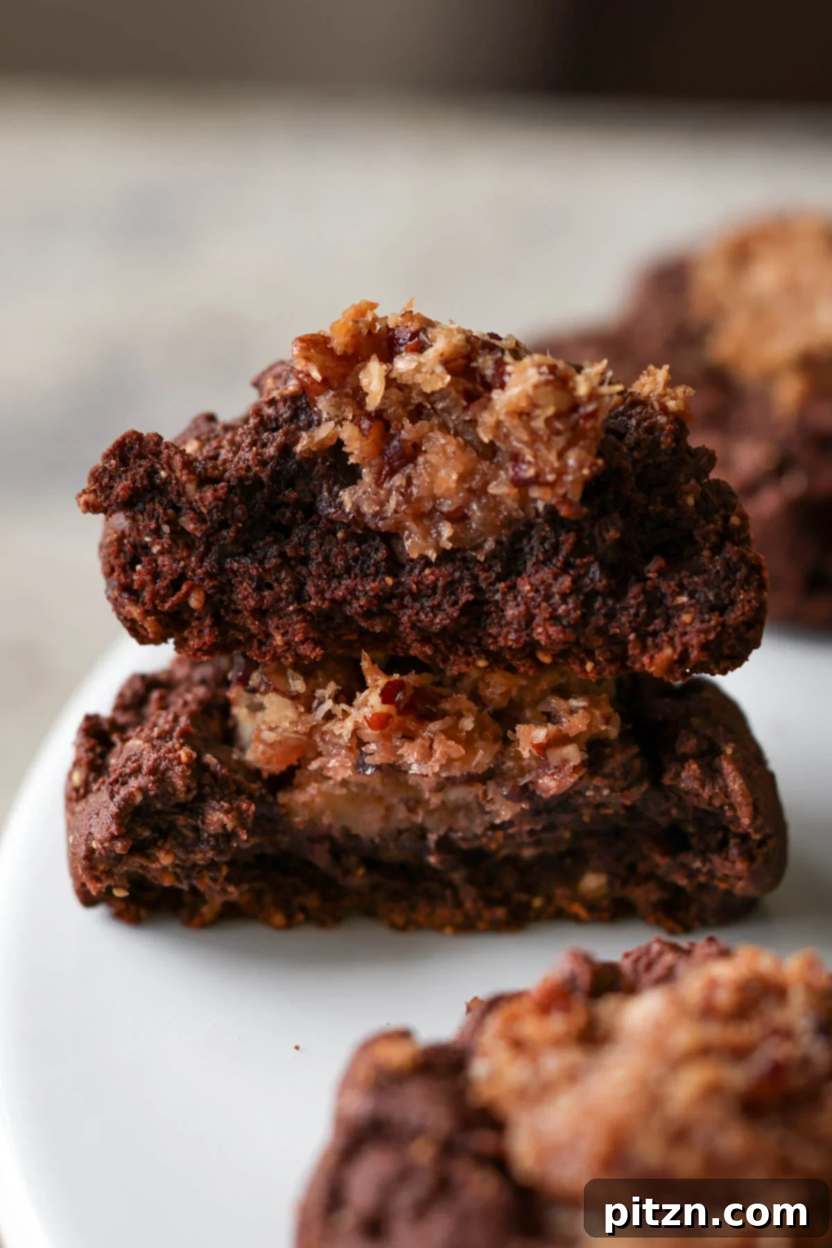 A vegan German chocolate cookie broken in half on a plate, revealing the generous, gooey caramel-coconut-pecan filling inside.