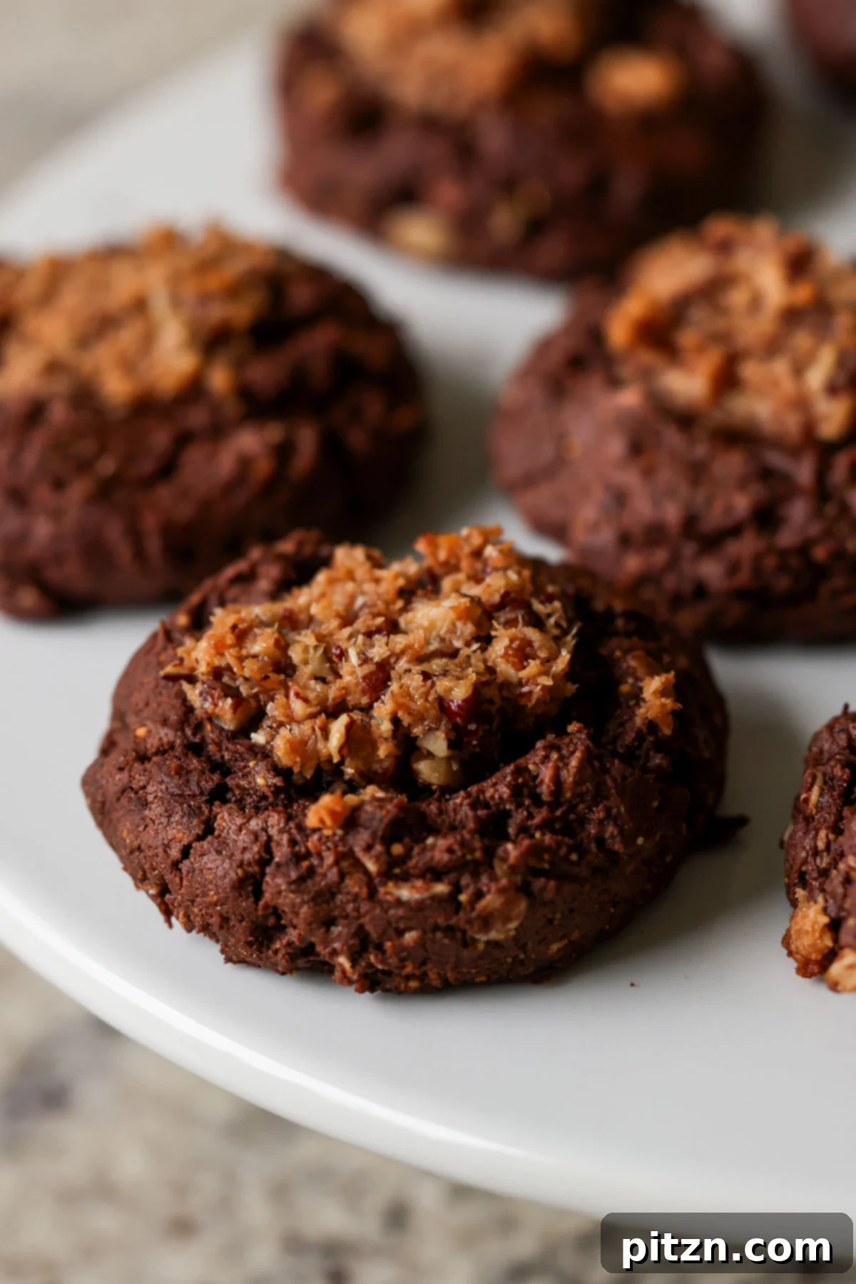 A single vegan German chocolate cookie resting on a white plate after baking, showcasing its inviting texture and golden-brown edges.
