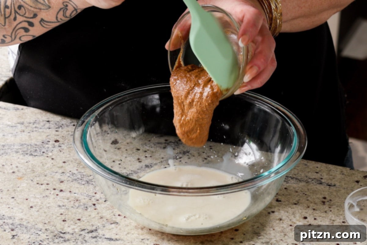 Wet ingredients being poured into the mixing bowl with dry ingredients, demonstrating the start of dough preparation.