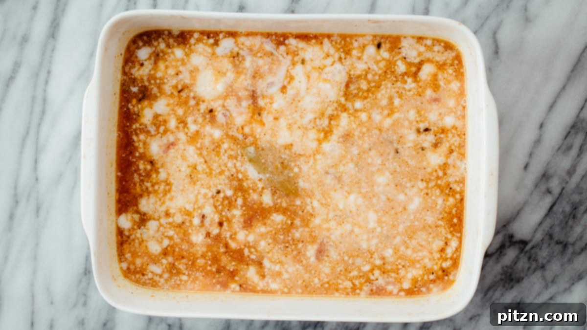 Adding Liquids to Casserole Coconut milk and vegetable broth being poured into a casserole dish already containing roasted spices, onions, and garlic.