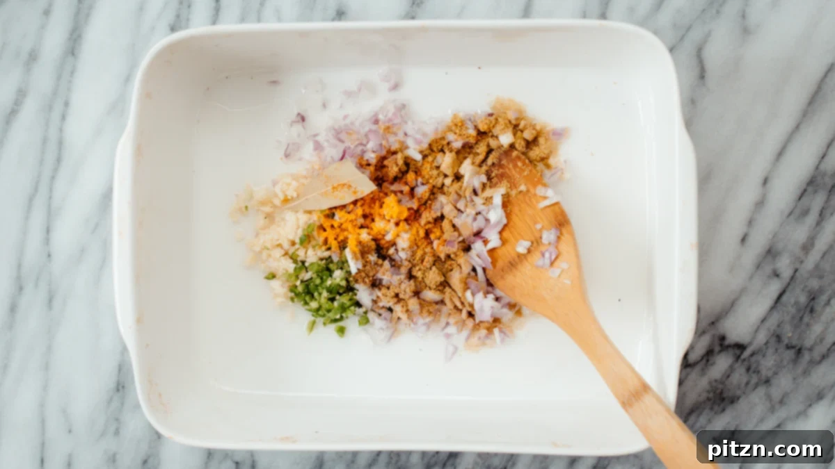 Onion, Garlic, Chili, Spices in Casserole A close-up view of finely chopped onion, minced garlic, green chili, and a blend of aromatic spices resting in a casserole dish.