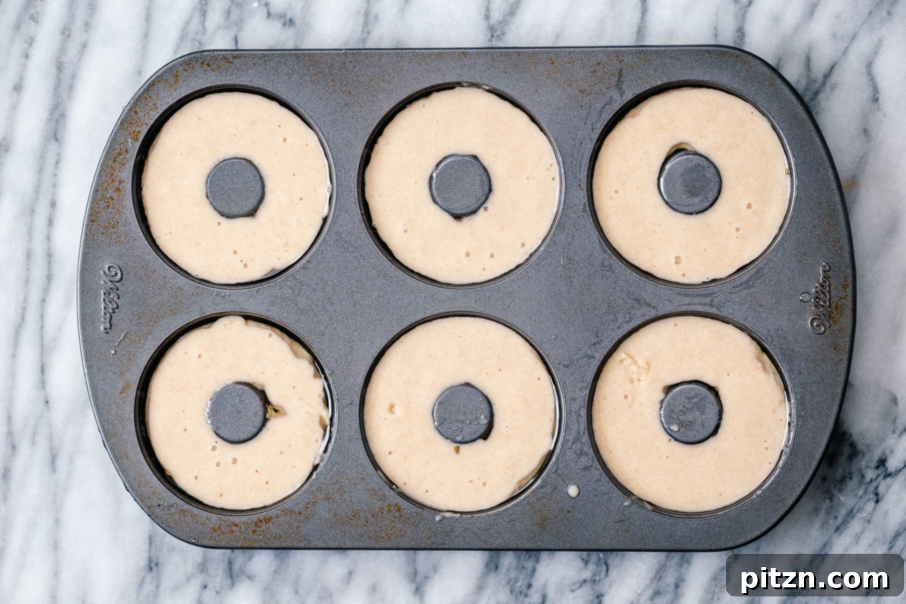 Filling Gluten-Free Donut Pan Hands carefully spooning the smooth gluten-free almond flour donut batter into a well-greased donut pan, preparing them for baking.
