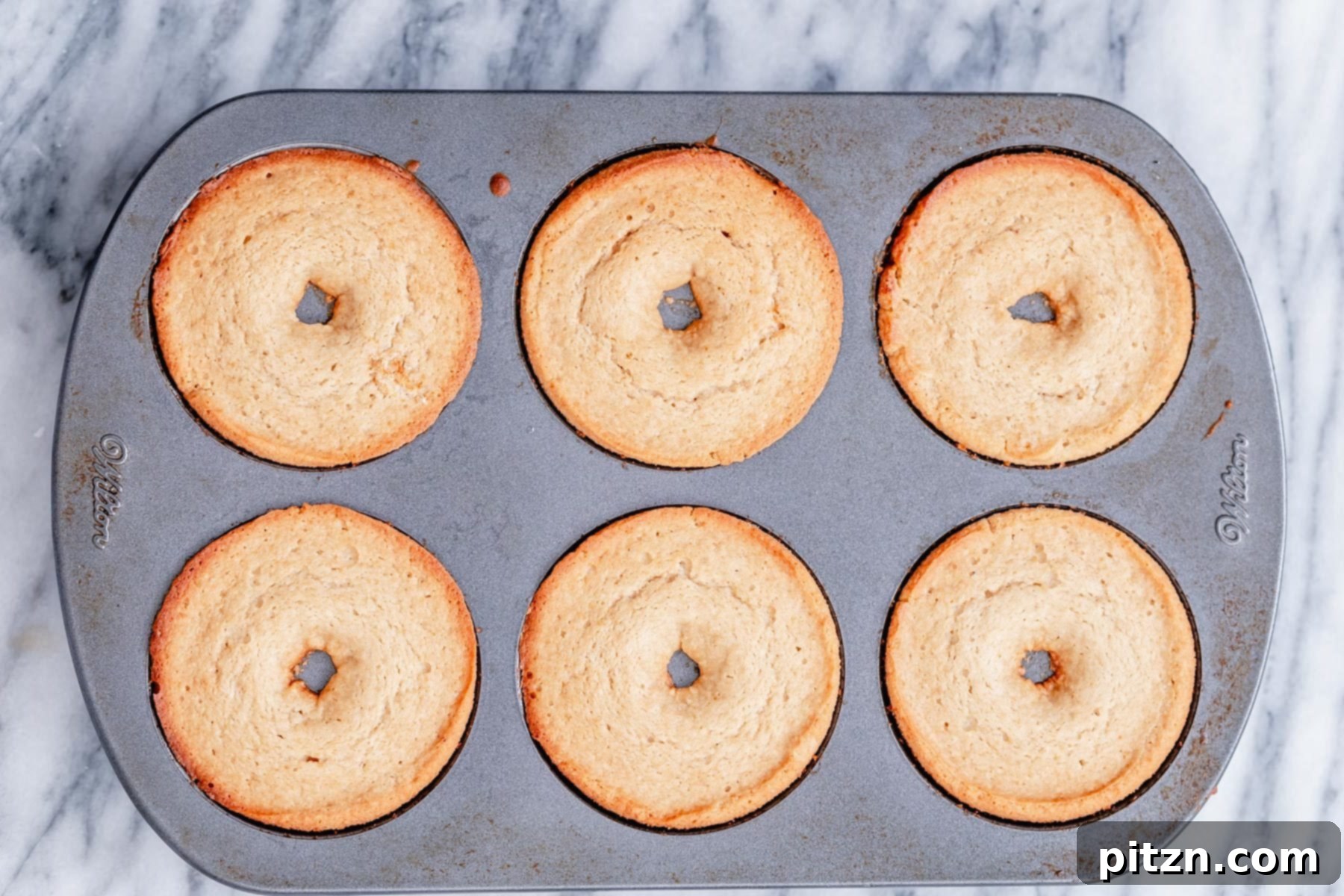 Freshly Baked Gluten-Free Donuts A metal baking pan filled with freshly baked, golden-brown gluten-free donuts, showcasing their beautiful shape and hinting at their soft texture right out of the oven.