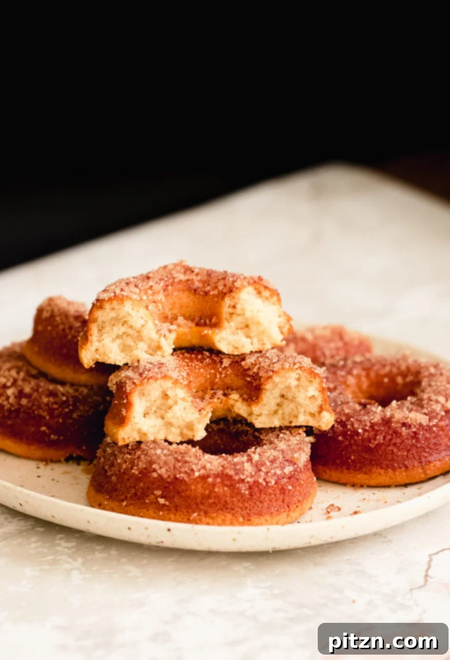 Moist Gluten-Free Donuts Recipe A close-up side view of a plate showcasing perfectly baked gluten-free vanilla donuts, with one donut thoughtfully cut in half to reveal its incredibly moist and airy interior texture. It's a tempting display of a healthy, delicious treat.