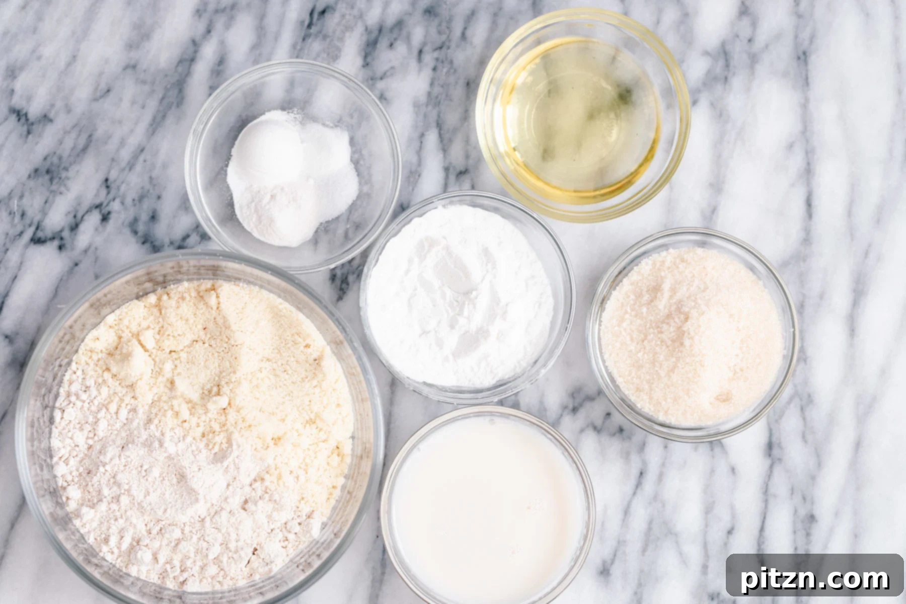 Ingredients for Gluten-Free Vanilla Donuts A flat lay photograph showcasing all the dry and wet ingredients neatly laid out on a clean surface, ready for mixing to create the gluten-free vanilla donuts recipe. Includes flours, sugar, oil, vanilla, and milk.