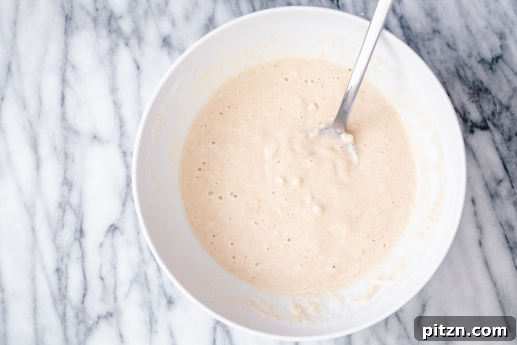 Gluten-Free Donut Batter Resting A perfectly smooth, light-colored gluten-free donut batter rests in a white mixing bowl, slightly thickened and expanded, indicating it's ready for baking.