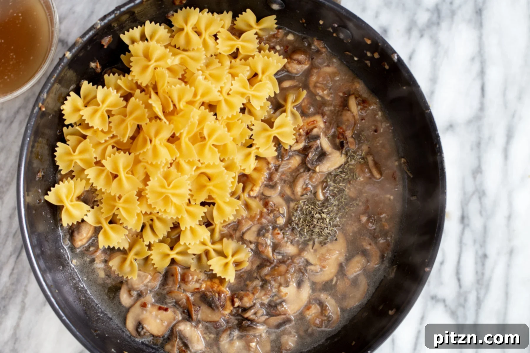 vegan mushroom stroganoff farfalle pasta being added to a pan with mushroom sauce