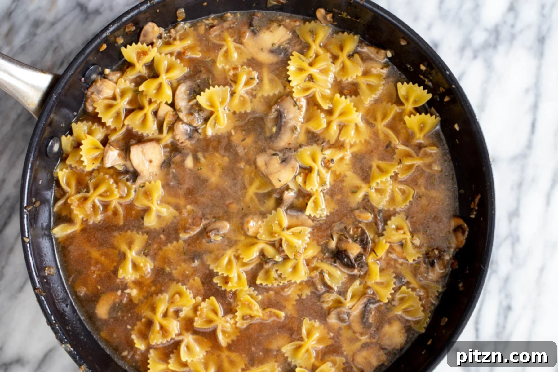 vegan mushroom stroganoff uncooked farafalle pasta and mushroom sauce cooking in a saucepan