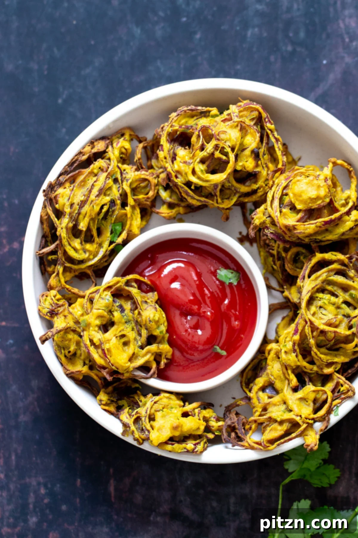 A beautiful platter featuring a generous serving of freshly baked onion pakora, artfully arranged around a small dish of ketchup, ready to be enjoyed. The pakoras are golden and inviting.