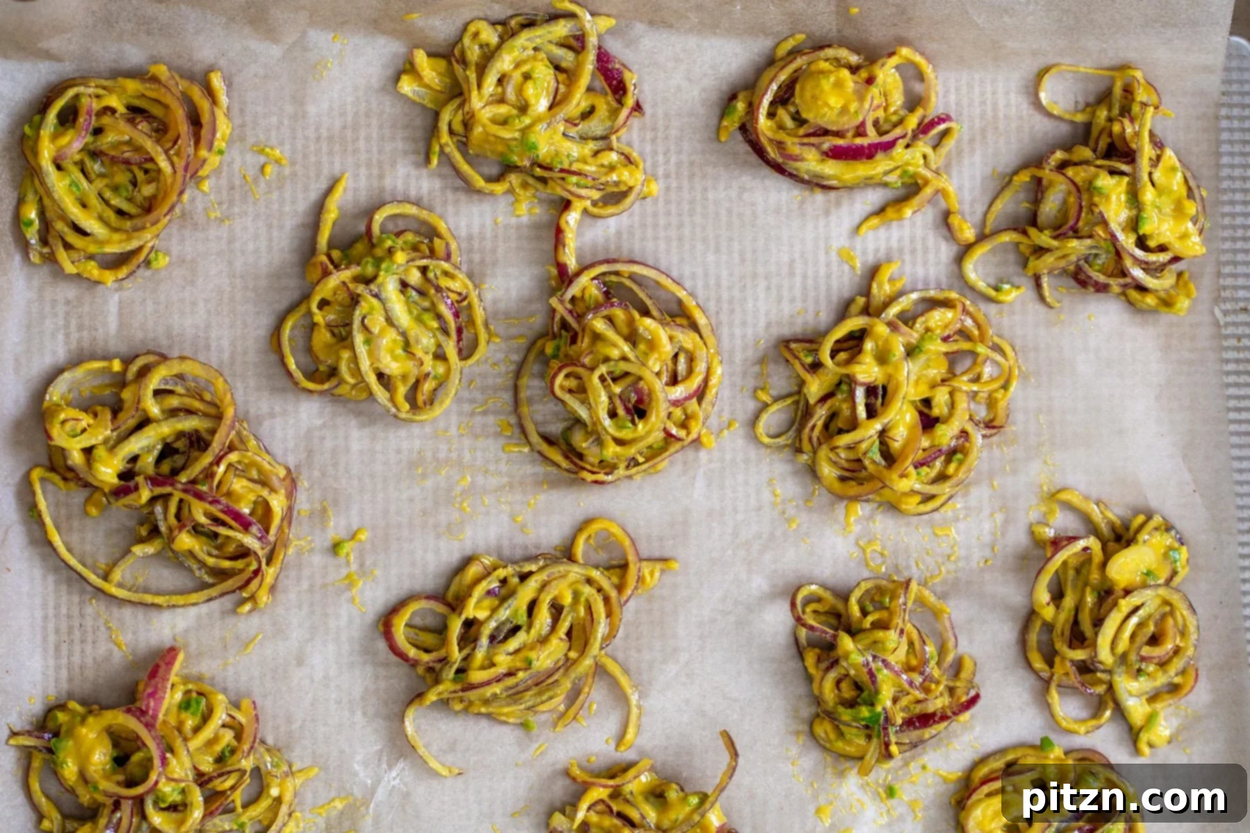 Close-up of small, perfectly formed mounds of spiced onion pakora batter being carefully placed onto a parchment-lined baking sheet, spaced evenly for optimal baking. This highlights the preparation stage before entering the oven.