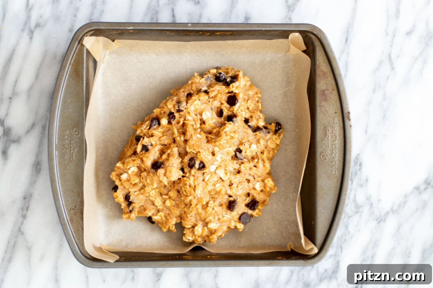 vegan date caramel oatmeal bar batter being added to a square baking pan 