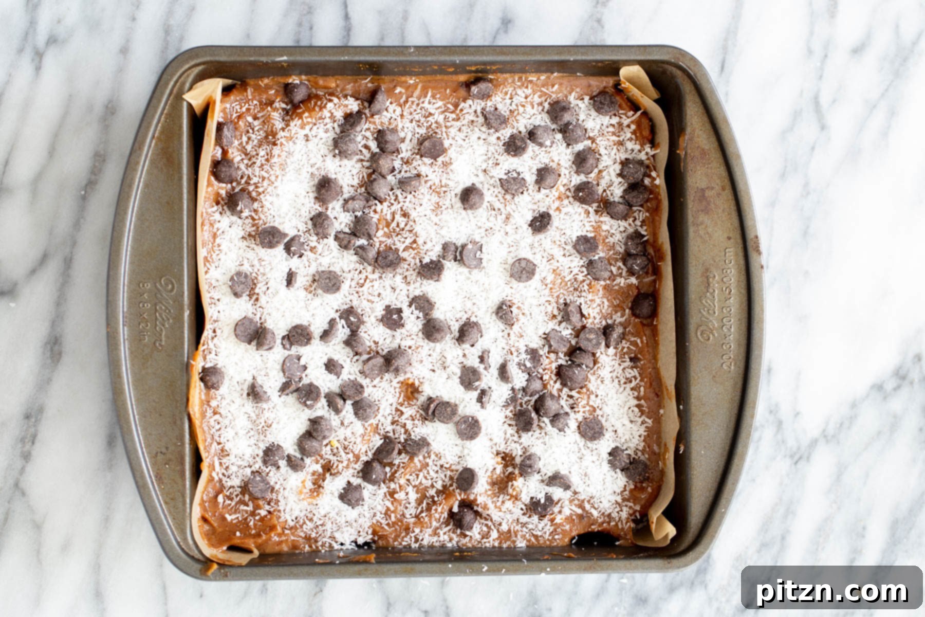 chocolate chips and shredded coconut being spread on top of oatmeal cookie base and date caramel to make caramel bars 