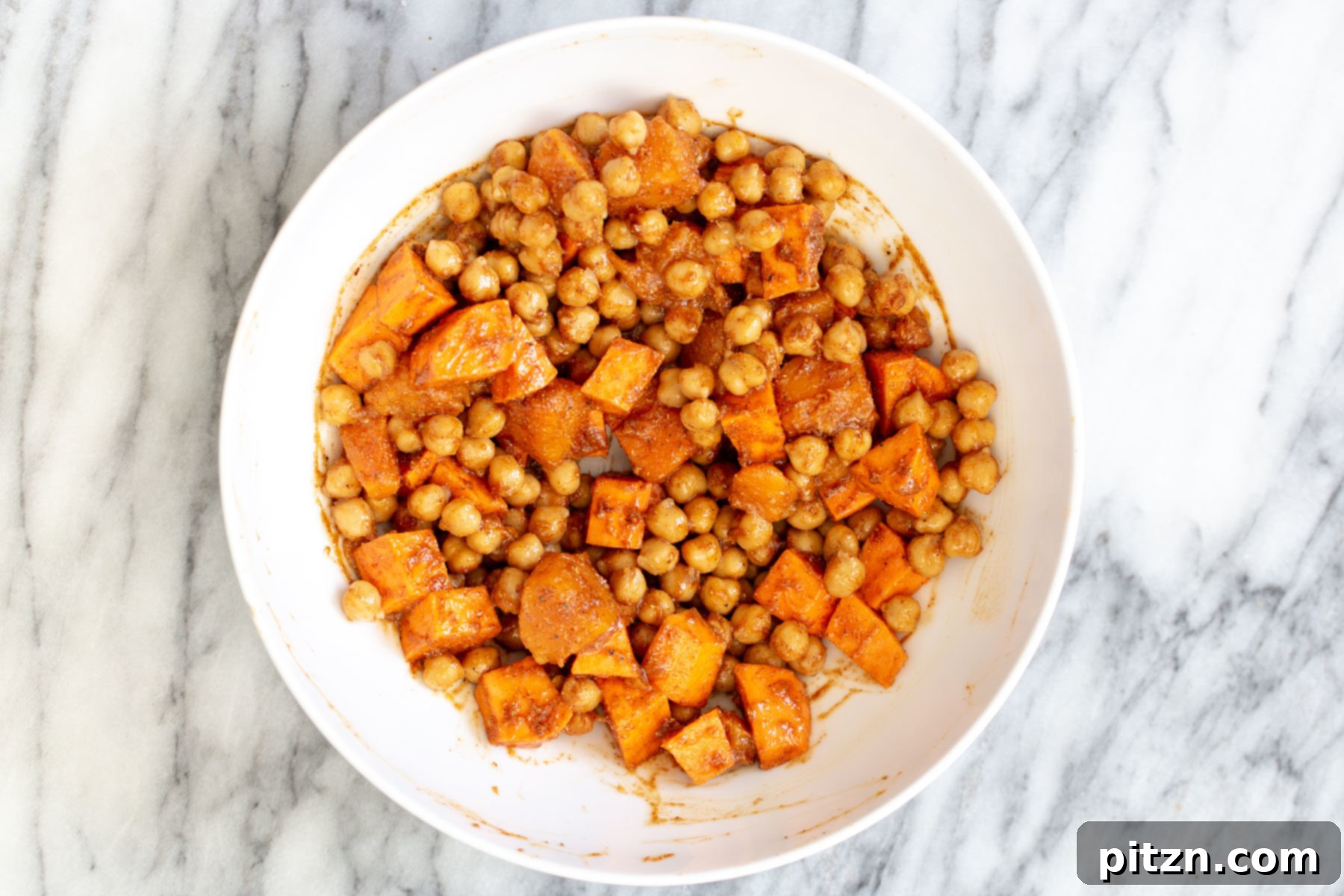 Cubed sweet potatoes and chickpeas thoroughly mixed with a fragrant blend of spices, ready for roasting.
