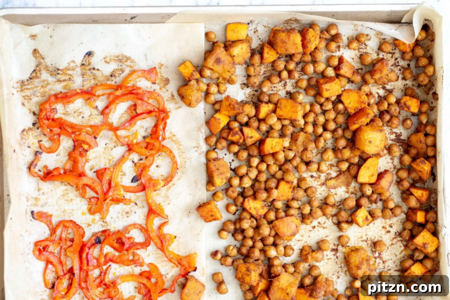 Chickpeas, sweet potatoes, and sliced red bell peppers spread on a sheet pan, ready for baking to create a vibrant vegan salad bowl.