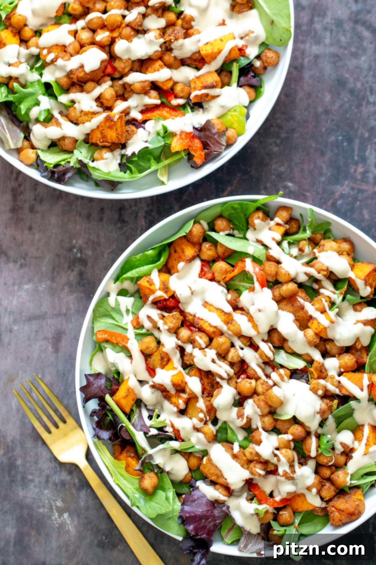 Two inviting bowls filled with fresh leafy greens, topped with a colorful mix of roasted chickpeas and tender cubed sweet potatoes.