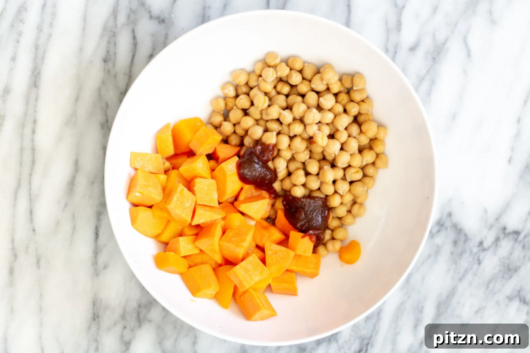 Cubed sweet potatoes and drained chickpeas in a bowl, coated with barbeque sauce and ready for seasoning.