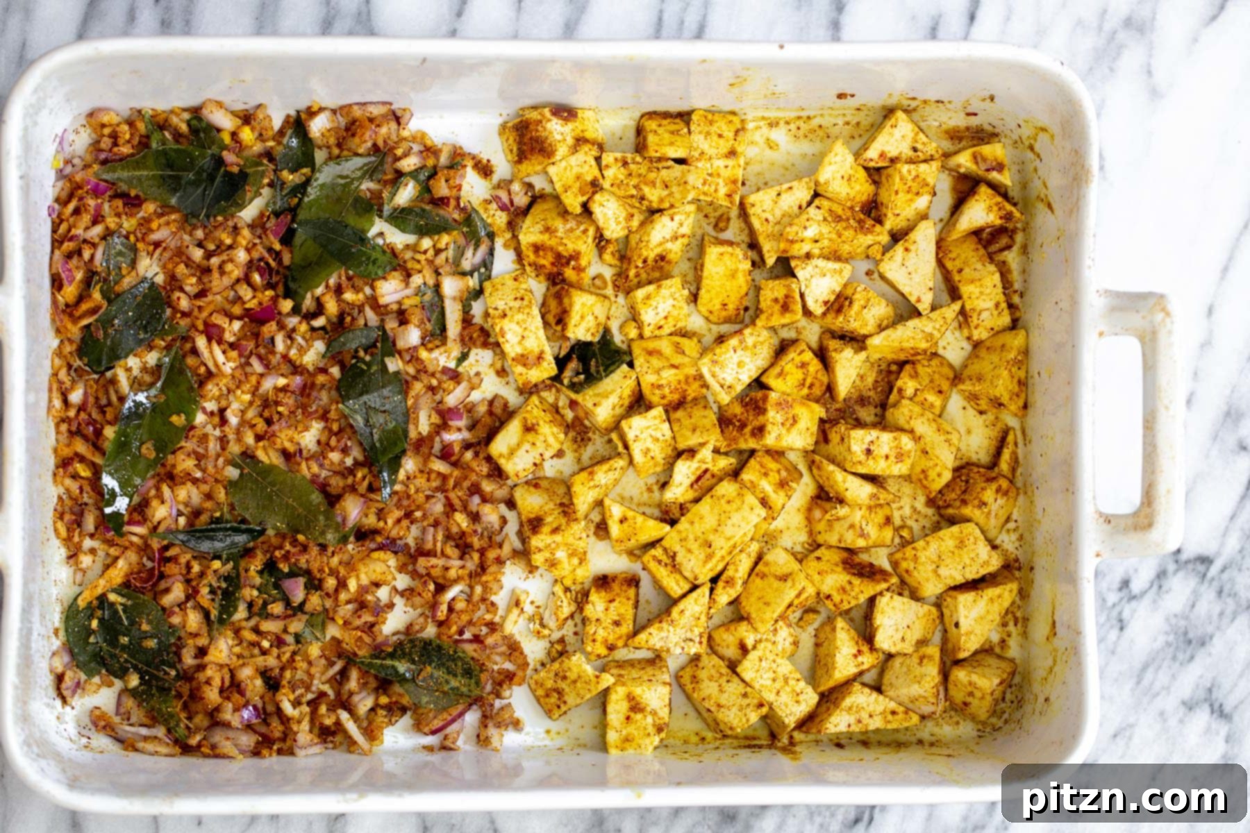 A casserole dish showcasing golden-brown, curry-spiced baked tofu alongside perfectly cooked, translucent onions.