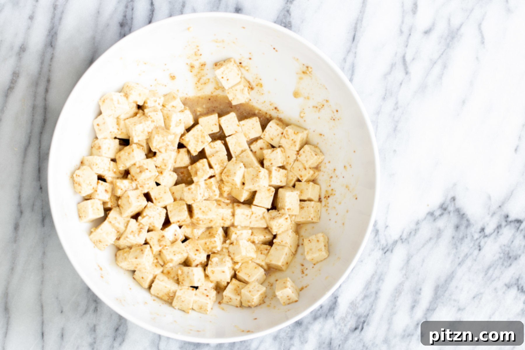 Spicy Maple Mustard Tofu and Sweet Potato Bowl 6 Marinated tofu cubes resting in a small white bowl, absorbing the spicy maple mustard flavors before coating.