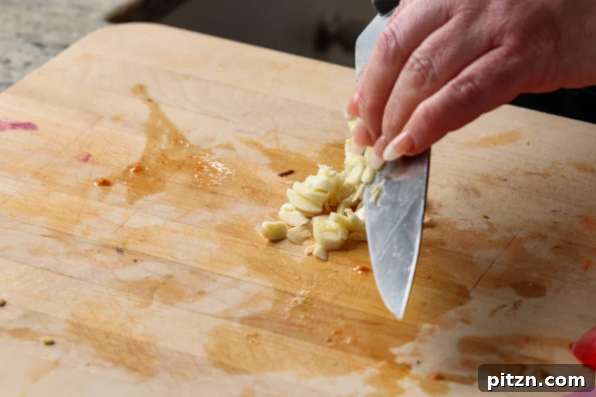 Fresh garlic cloves being finely minced on a cutting board, an essential aromatic for the Italian dressing.