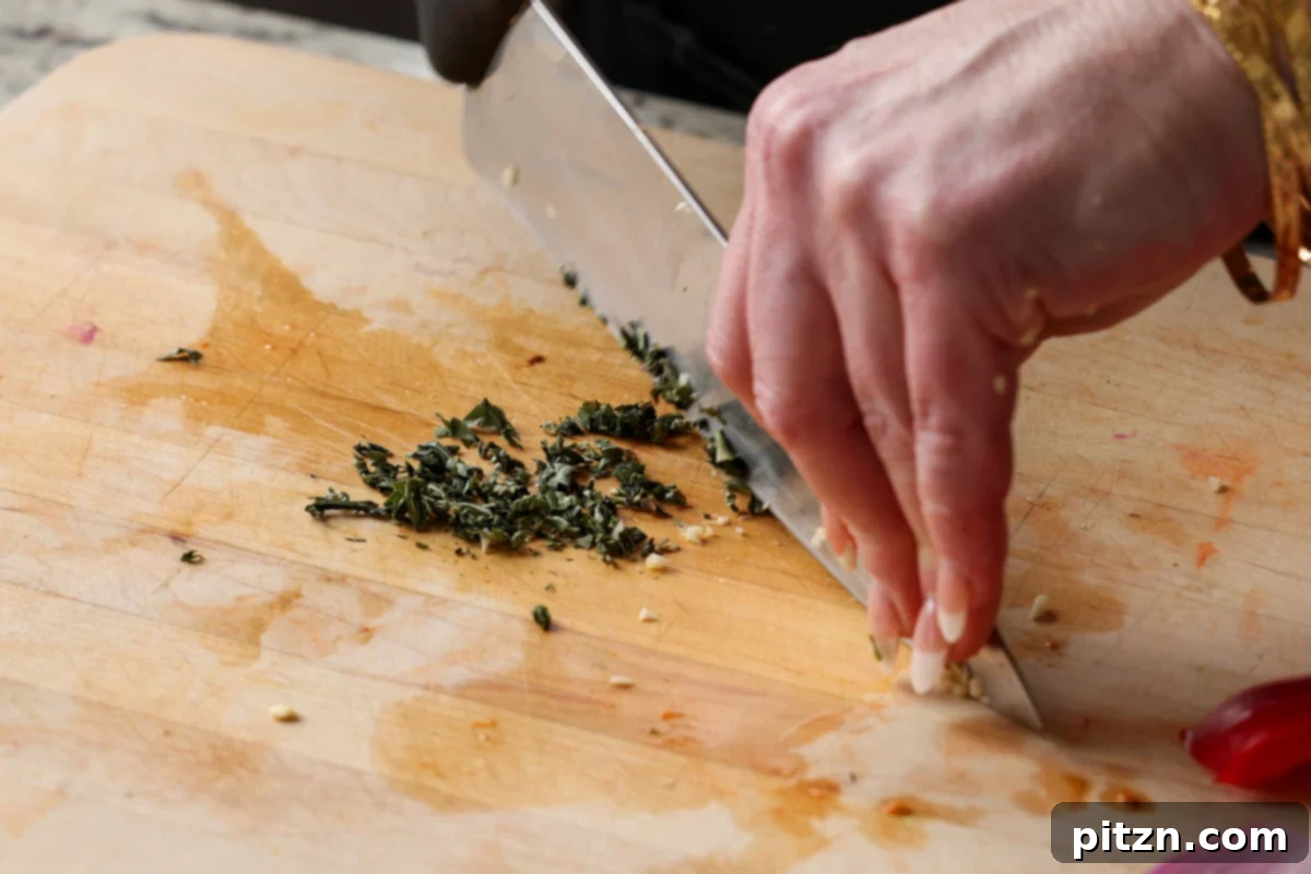Fresh basil leaves being finely minced on a cutting board, adding aromatic freshness to the dressing.