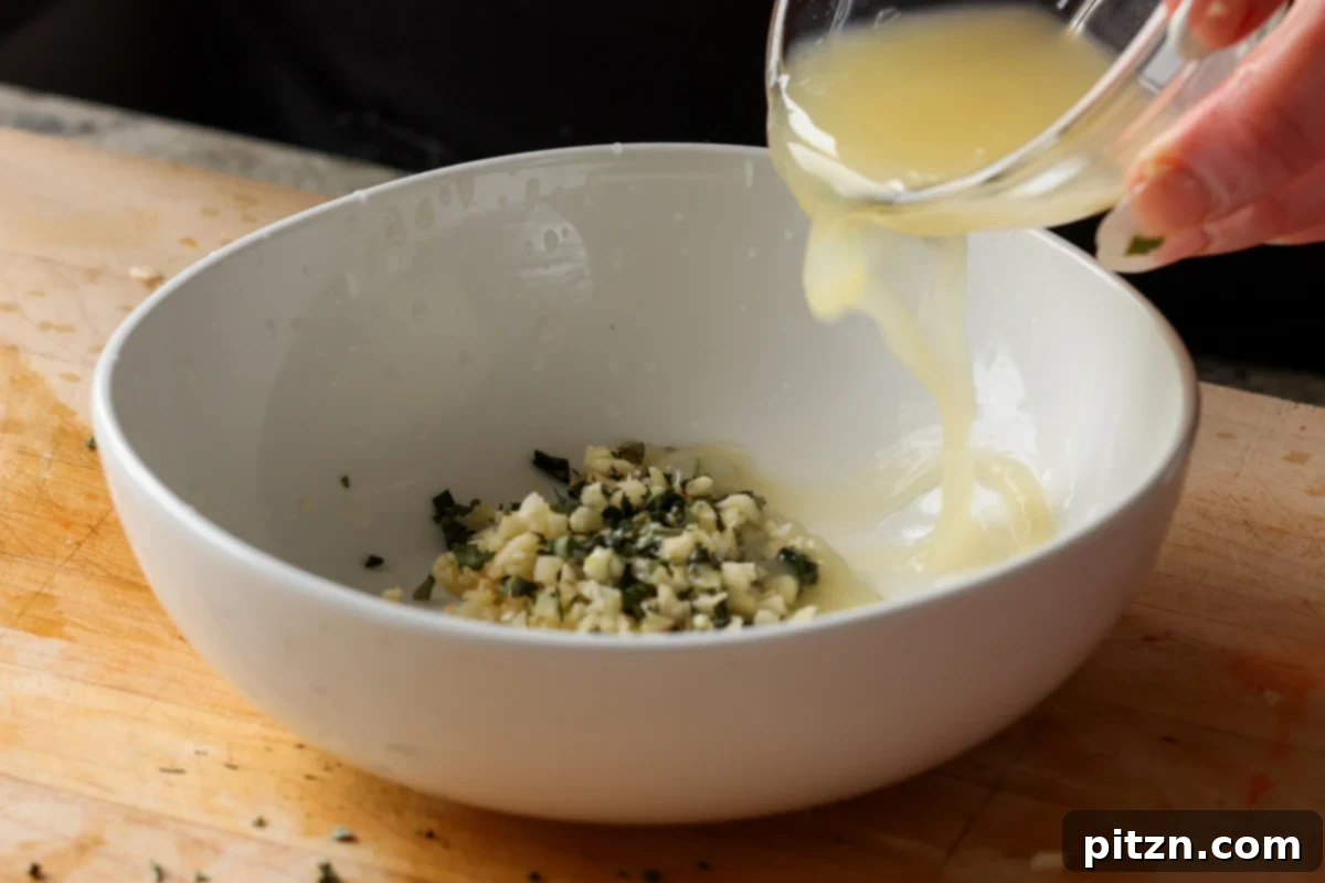 Freshly squeezed lemon juice being added to a bowl with minced garlic and herbs, forming the base of the zesty dressing.