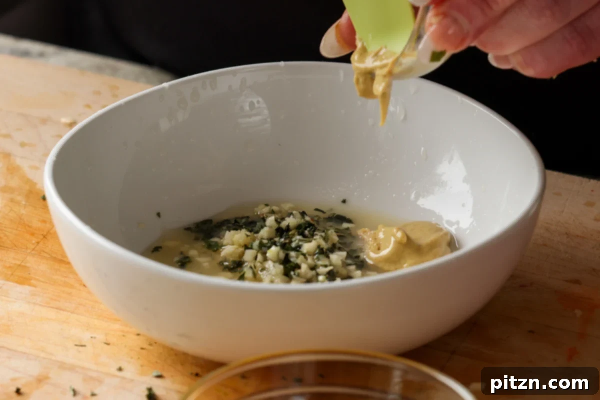 A spoonful of Dijon mustard being added to the dressing ingredients in a bowl, contributing a tangy depth of flavor.